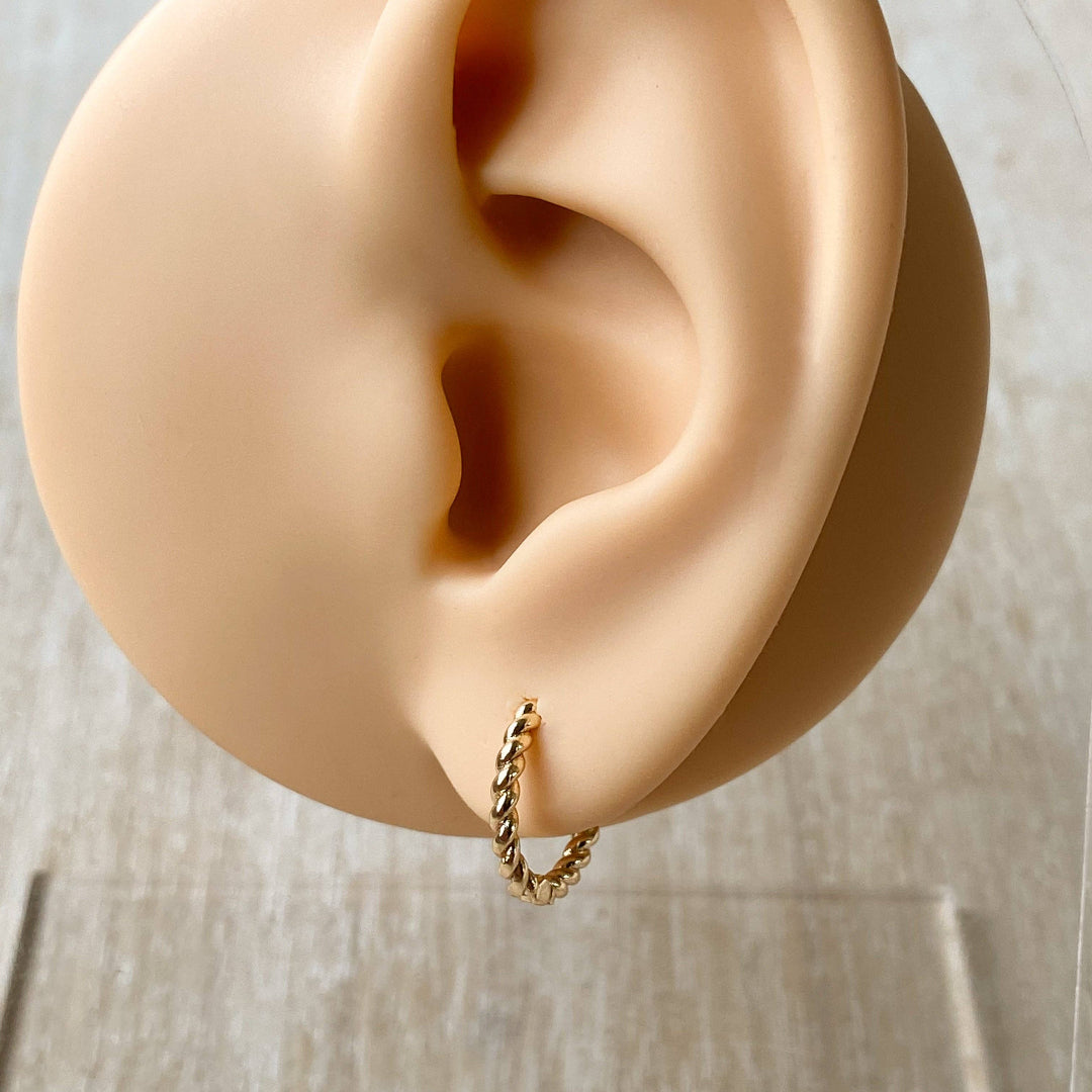 Gold hoop earring worn on a mannequin ear against a neutral background