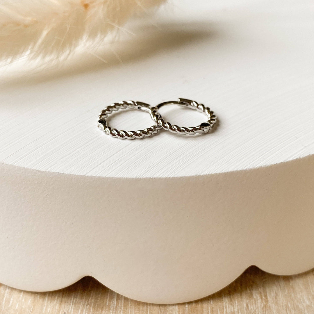 Two silver hoop earrings on a white shell