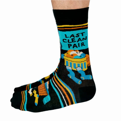 A pair of black socks with a laundry-themed design. The socks feature a washing machine, detergent bottles, a laundry basket, and socks themselves. It reads 