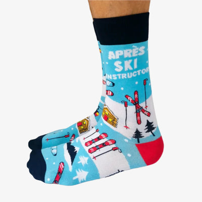 A pair of blue socks with a winter sports theme. The socks feature illustrations of skiers, snowboards, and a mountain cabin. The text 