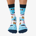 A pair of blue socks with a winter sports theme. The socks feature illustrations of skiers, snowboards, and a mountain cabin. The text "Après Ski Instructor" is printed on the socks.