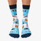 A pair of blue socks with a winter sports theme. The socks feature illustrations of skiers, snowboards, and a mountain cabin. The text 