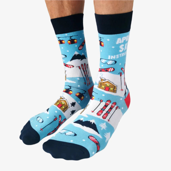 A pair of blue socks with a winter sports theme. The socks feature illustrations of skiers, snowboards, and a mountain cabin. The text 