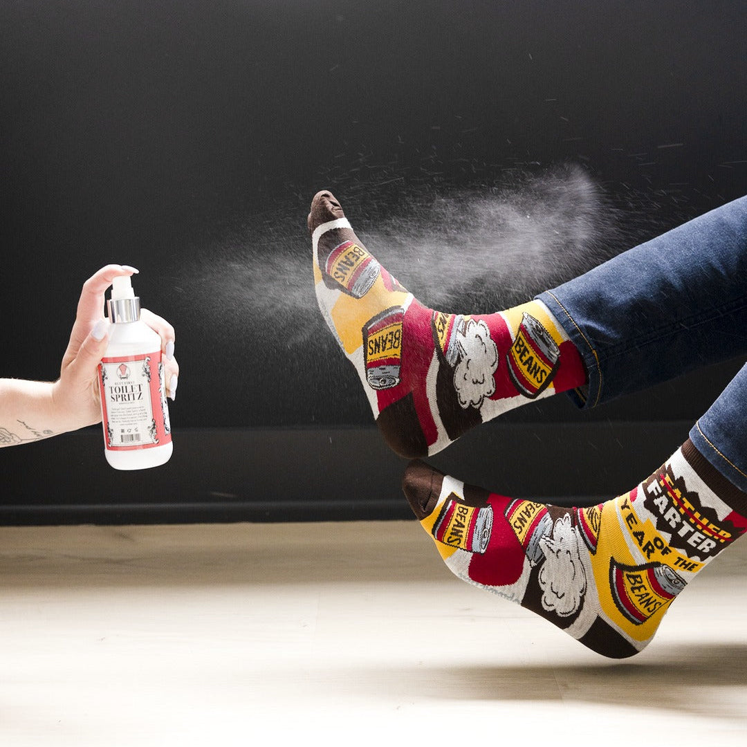 Person wearing colorful socks with brand logos, getting a spray on their foot against a black background.