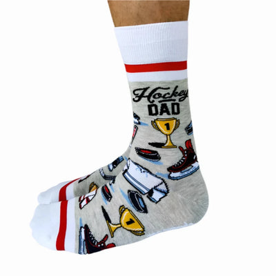 A pair of crew socks featuring a hockey theme. The socks are mostly grey with white and red stripes at the top and bottom. The design includes hockey-related icons like a trophy, skates, and a puck. The text 