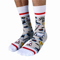 A pair of crew socks featuring a hockey theme. The socks are mostly grey with white and red stripes at the top and bottom. The design includes hockey-related icons like a trophy, skates, and a puck. The text "Hockey Dad" is printed on the socks.