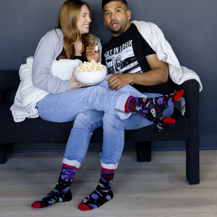 A pair of black socks with a Halloween-themed design. The socks feature a zombie hand, skulls, tombstones, and the phrase 