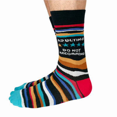 A pair of crew socks with a humorous message. The socks are mostly black with colorful stripes. The text 