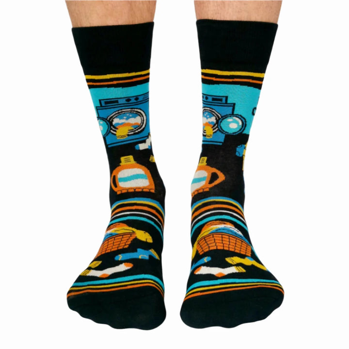 A pair of black socks with a laundry-themed design. The socks feature a washing machine, detergent bottles, a laundry basket, and socks themselves. It reads 