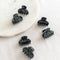 Six small, black hair claw clips arranged on a white marble surface. The clips have a marbled texture.