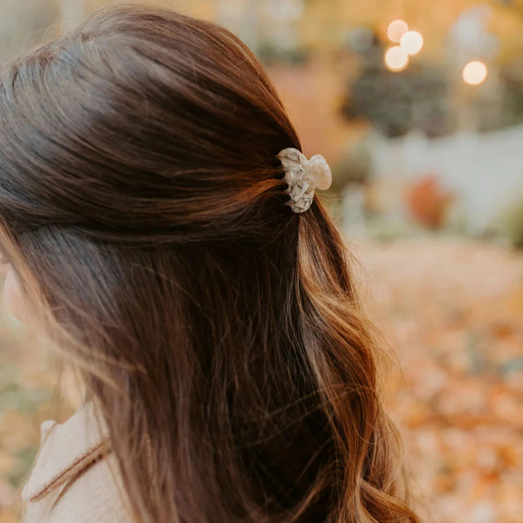 A small cream hair claw clip modeled in a persons hair.