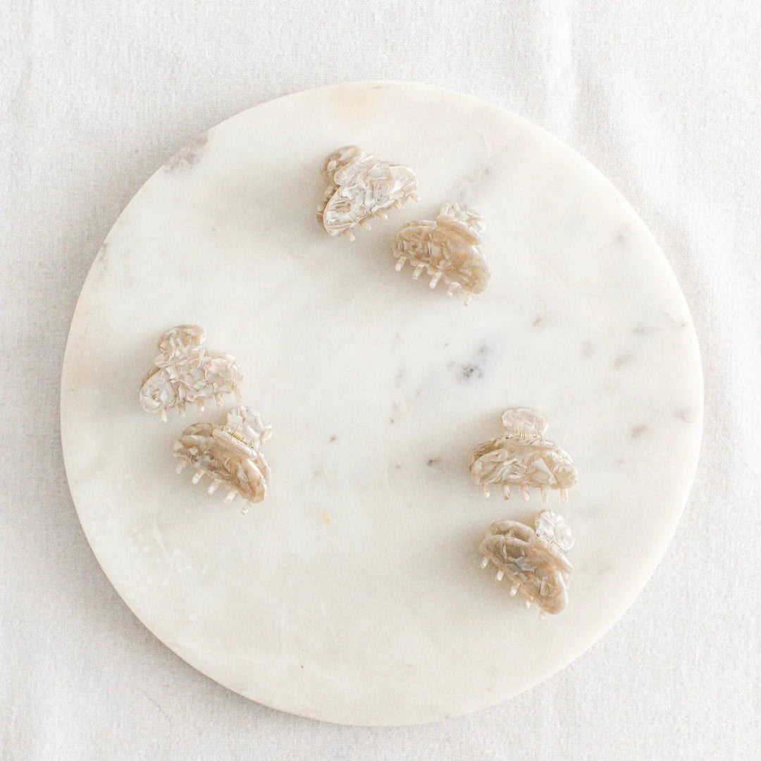 Six small, creamy hair claw clips arranged on a white marble surface. The clips have a marbled texture.