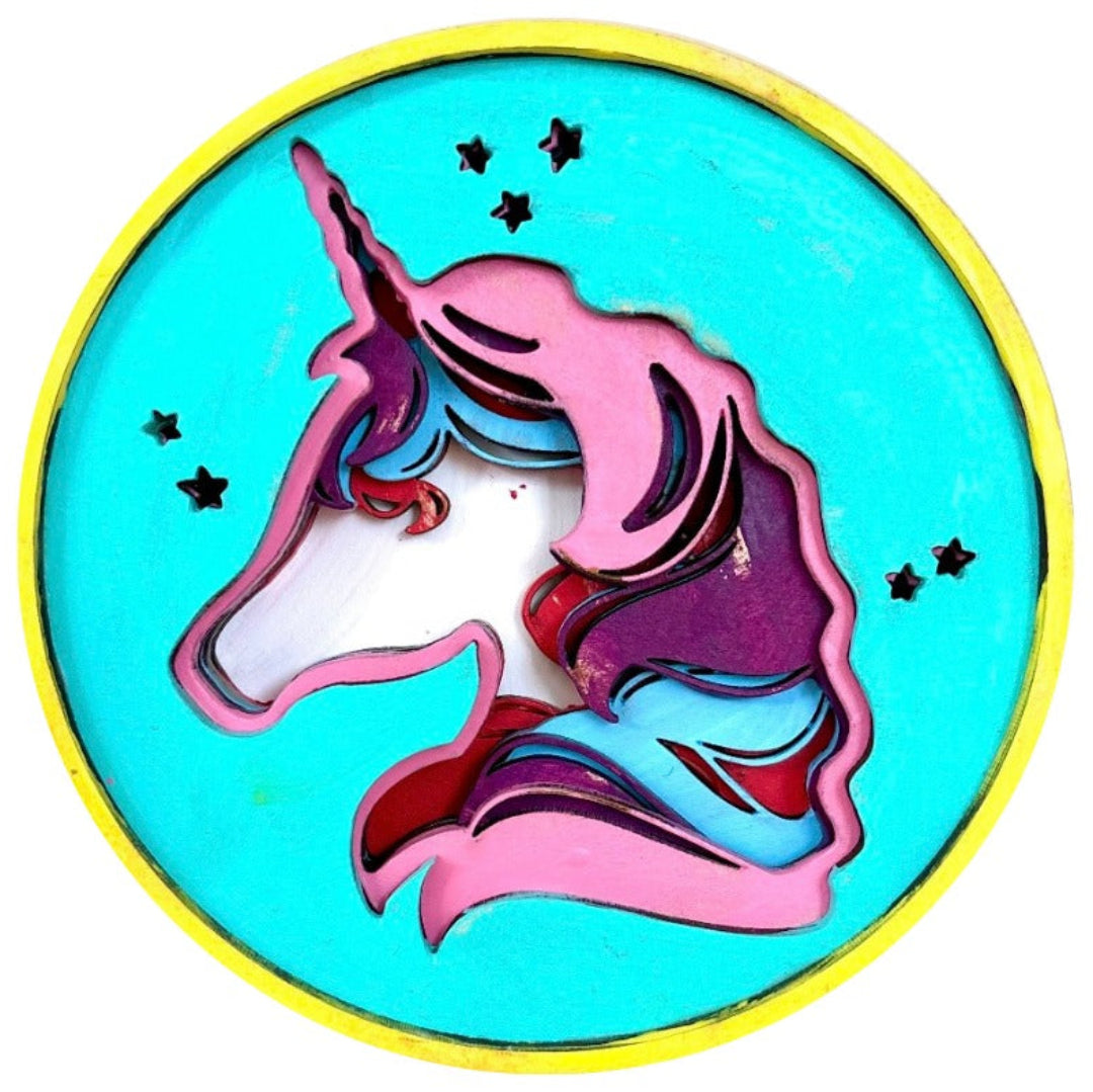 A circular decorative plaque or sign featuring a stylized unicorn head in pink, purple, blue, and white, set against a bright turquoise background with a yellow border and small black stars.