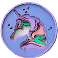 A circular wooden wall plaque featuring a layered, laser-cut unicorn head design with a purple horn and mane, set against a light purple background with small star cutouts.