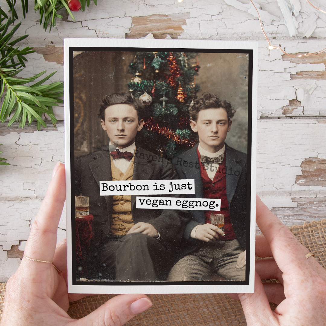 Two men holding a glass with text 'Bourbon is just vegan eggnog' against a Christmas tree background.