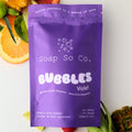 Purple package of Soap So Co. Bubbles Violet with fruits in the background