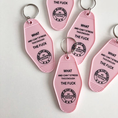 A collection of pink motel-style key tags scattered on a white surface. Each tag features bold black text that reads 