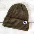 Green knit beanie with a logo on a light wooden background