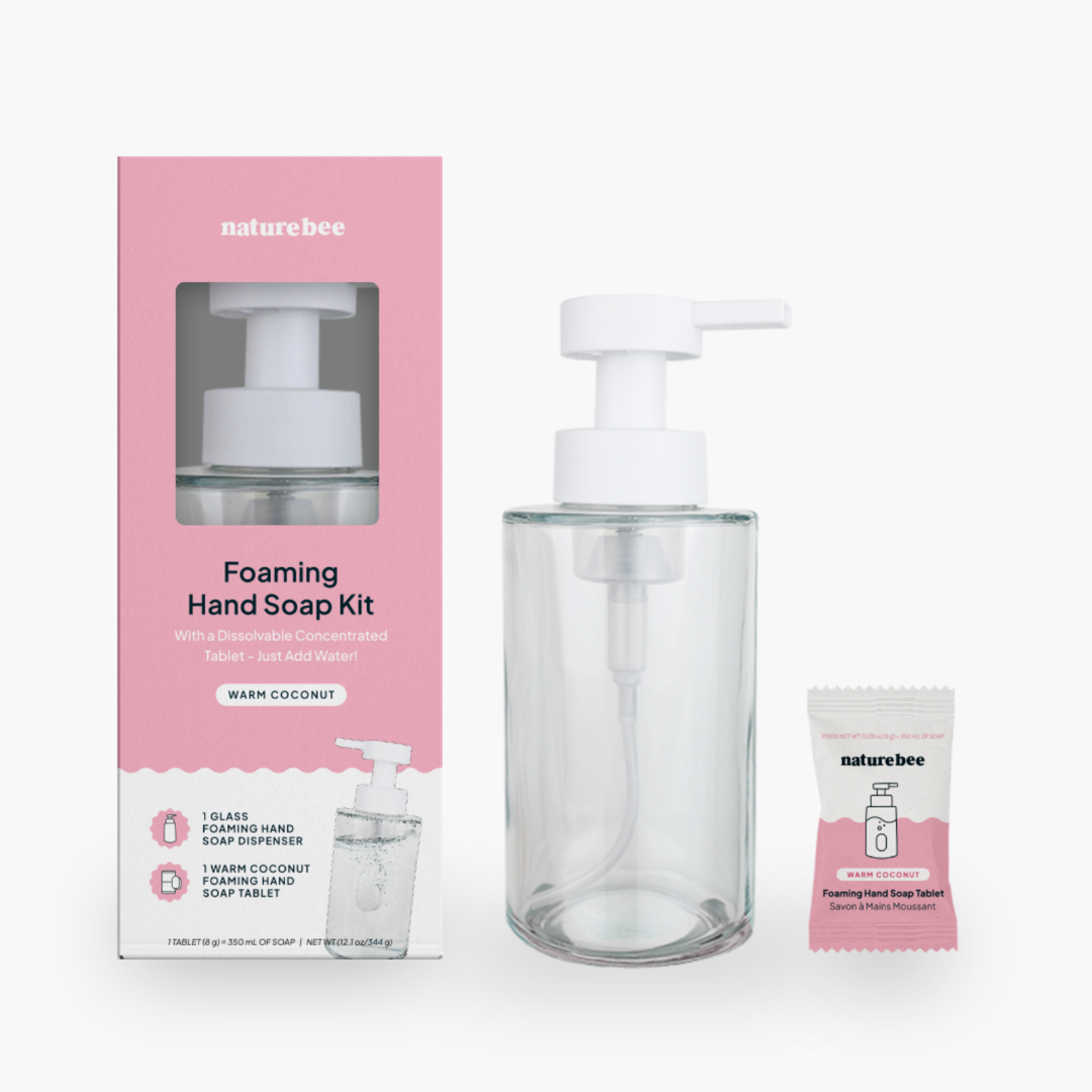 A Warm Coconut Foaming Hand Soap Kit by Nature Bee. The kit includes a pink and white box, a clear glass foaming hand soap dispenser with a white pump, and a small, individual packet of the Warm Coconut foaming hand soap tablet.