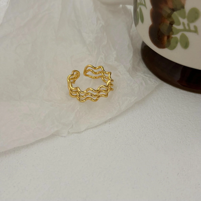 A wave ring made with 18K gold plating, featuring a modern, abstract, and undulating triple wave design, displayed on a light, textured surface. This unique ring is available in Ottawa, Ontario, Canada.