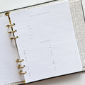 A blue agenda with a floral design. The cover features large red poppies, pink flowers, and green leaves against a blue background. The word "AGENDA" is printed in gold foil on the cover, along with the brand name "IDLEWILD CO." The agenda has a pink elastic band.