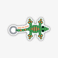 A playful sticker shaped like a green and orange beaded lizard. It has a ring at its tail end with the text "What the geck?" written in orange on a curved line. The entire sticker is outlined in black.