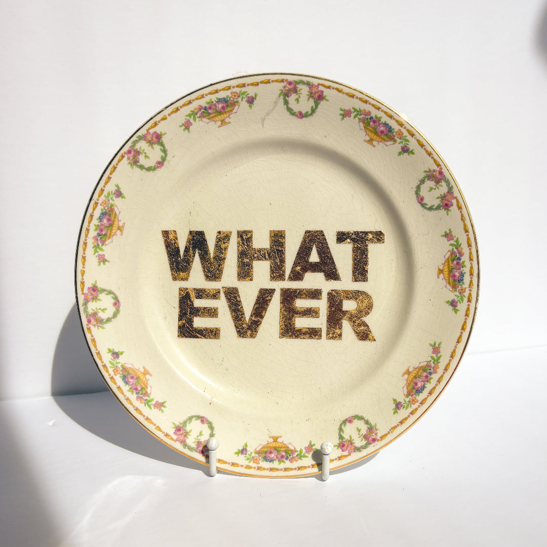 Decorative plate with floral rim and 'WHAT EVER' text on a white background
