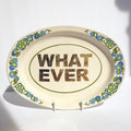 Decorative plate with 'WHAT EVER' text and floral design on a stand.