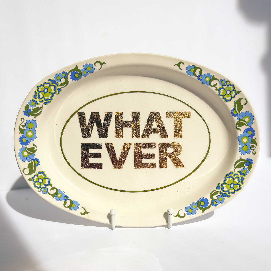 Decorative plate with 'WHAT EVER' text and floral design on a stand.