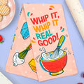 Colorful kitchen towel with 'WHIP IT, WHIP IT REAL GOOD!' text and kitchen-themed graphics on a light blue background.