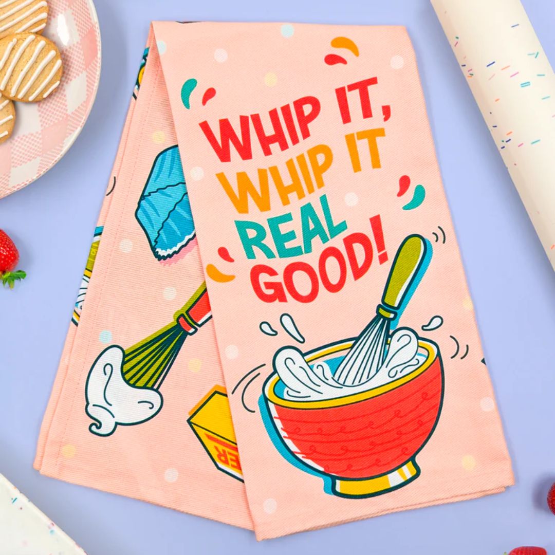 Colorful kitchen towel with 'WHIP IT, WHIP IT REAL GOOD!' text and kitchen-themed graphics on a light blue background.