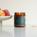 Candle jar with a label next to peaches on a white surface