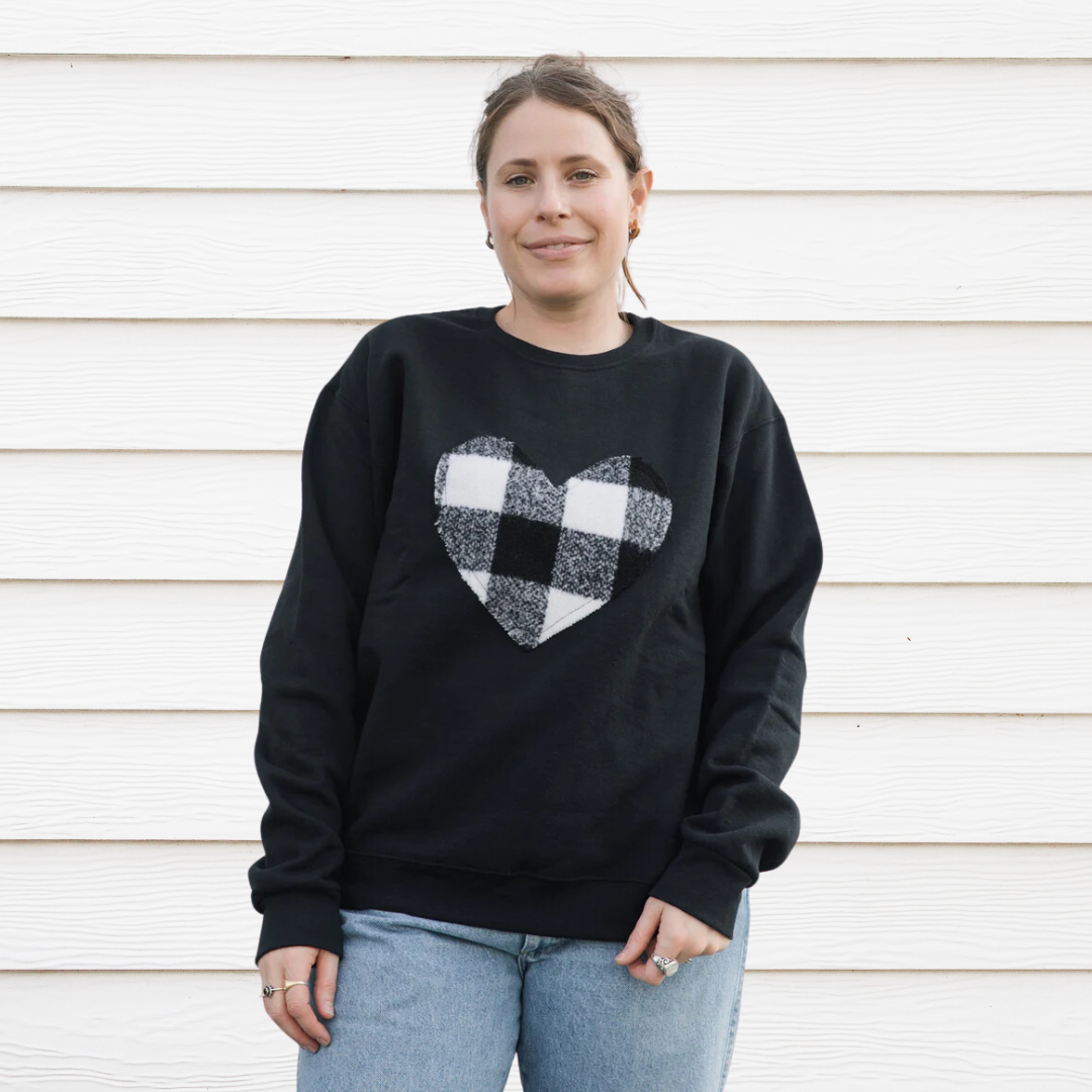 A black sweatshirt with a large, white and black buffalo plaid heart design in the center.