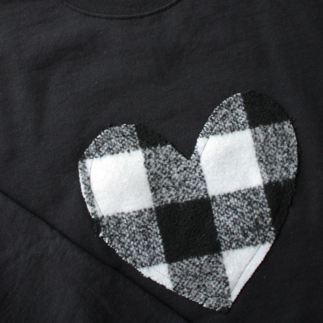 A black sweatshirt with a large, white and black buffalo plaid heart design in the center.