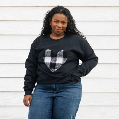 A black sweatshirt with a large, white and black buffalo plaid heart design in the center.