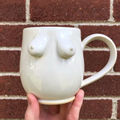 White ceramic mug with abstract design held against a brick wall.
