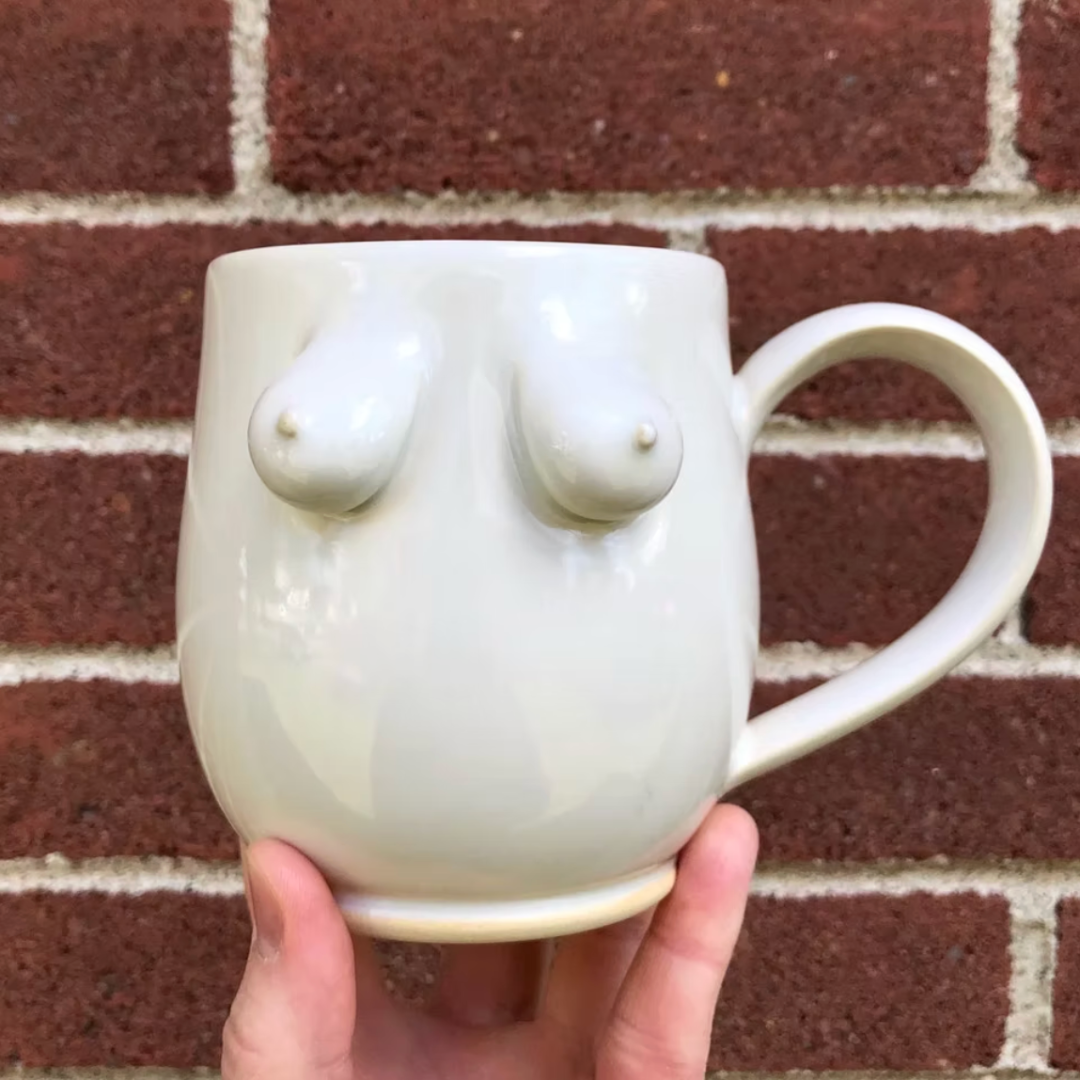 White ceramic mug with abstract design held against a brick wall.