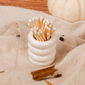 White ceramic container with matches on a beige surface with pumpkins and cinnamon sticks.