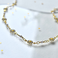 A delicate gold chain necklace adorned with small white daisies. The daisies have yellow centers and are evenly spaced along the chain.