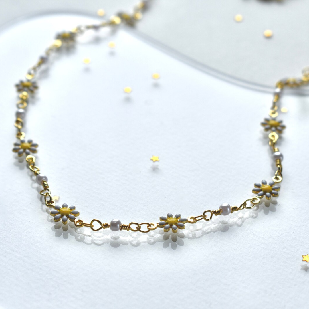 A delicate gold chain necklace adorned with small white daisies. The daisies have yellow centers and are evenly spaced along the chain.