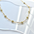 A delicate gold chain necklace adorned with small white daisies. The daisies have yellow centers and are evenly spaced along the chain.