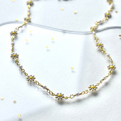 A delicate gold chain necklace adorned with small white daisies. The daisies have yellow centers and are evenly spaced along the chain.
