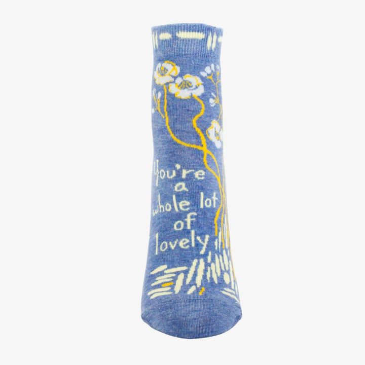 A pair of light blue ankle socks with a pattern of white and yellow flowers and branches. One sock features the text 