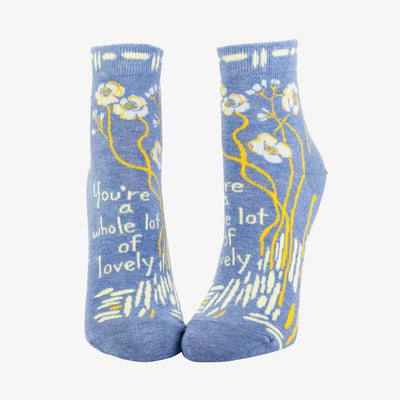 A pair of light blue ankle socks with a pattern of white and yellow flowers and branches. One sock features the text 
