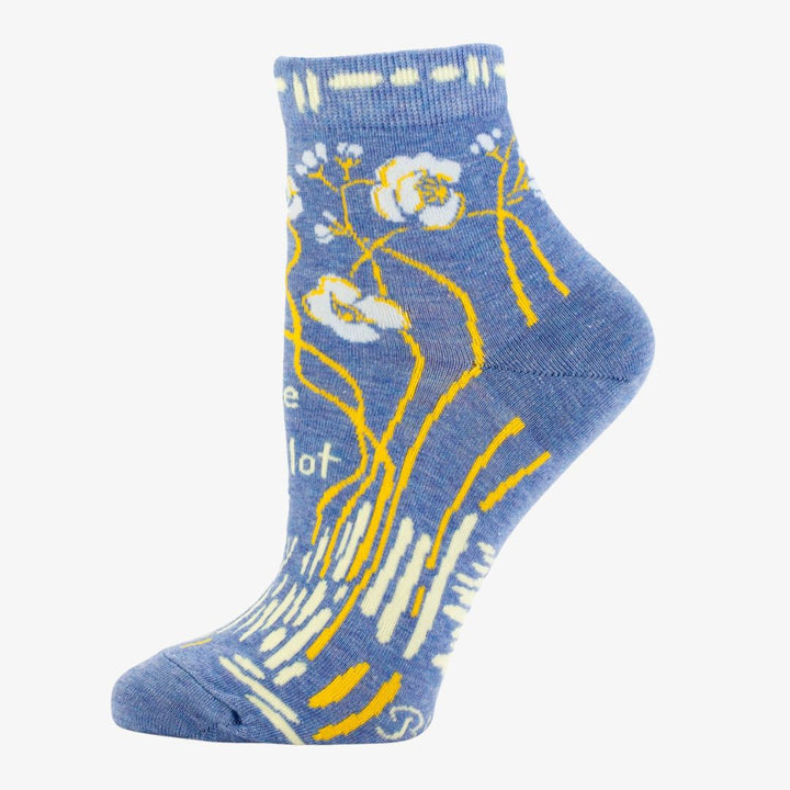 A pair of light blue ankle socks with a pattern of white and yellow flowers and branches. One sock features the text 