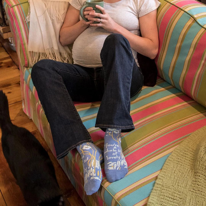 A pair of light blue ankle socks with a pattern of white and yellow flowers and branches. One sock features the text 