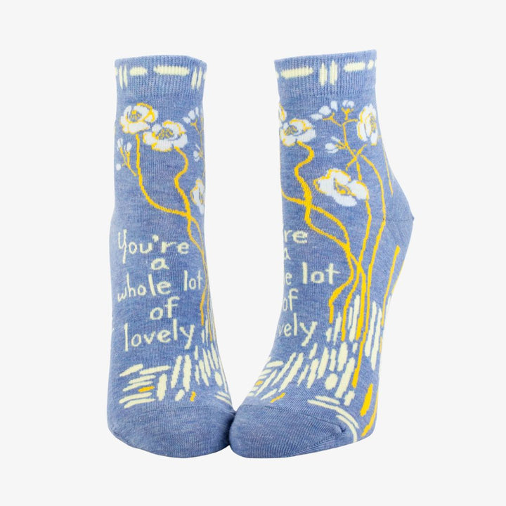 A pair of light blue ankle socks with a pattern of white and yellow flowers and branches. One sock features the text 