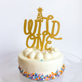 Small white cake with colorful sprinkles and a gold 'Wild One' topper on a white background