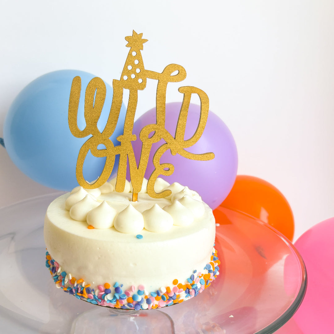 Small birthday cake with 'Happy One' topper and colorful balloons in the background