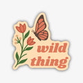 A whimsical sticker with a wavy light cream background and a thick black outline. It features a stylized plant with green stems, red-orange tulip-like flowers, and small beige berries on the left. On the right, a butterfly with red-orange wings and a brown body flies above the stacked text "wild thing" in a matching red-orange font.